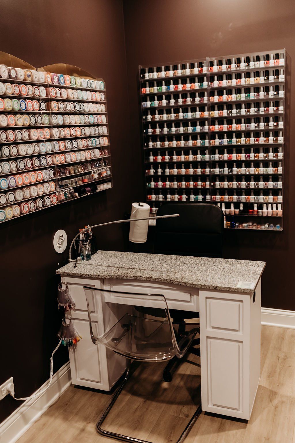 A nail salon with a desk , chair , and lots of nail polish on the wall.