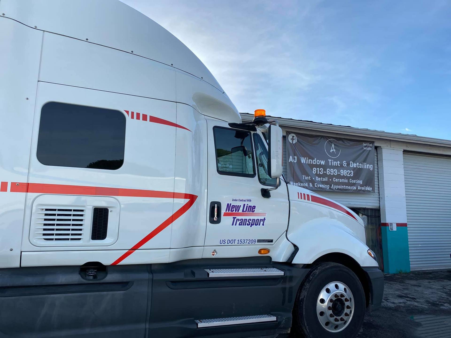 White semi-truck with red stripes parked in front of a building; daytime shot.
