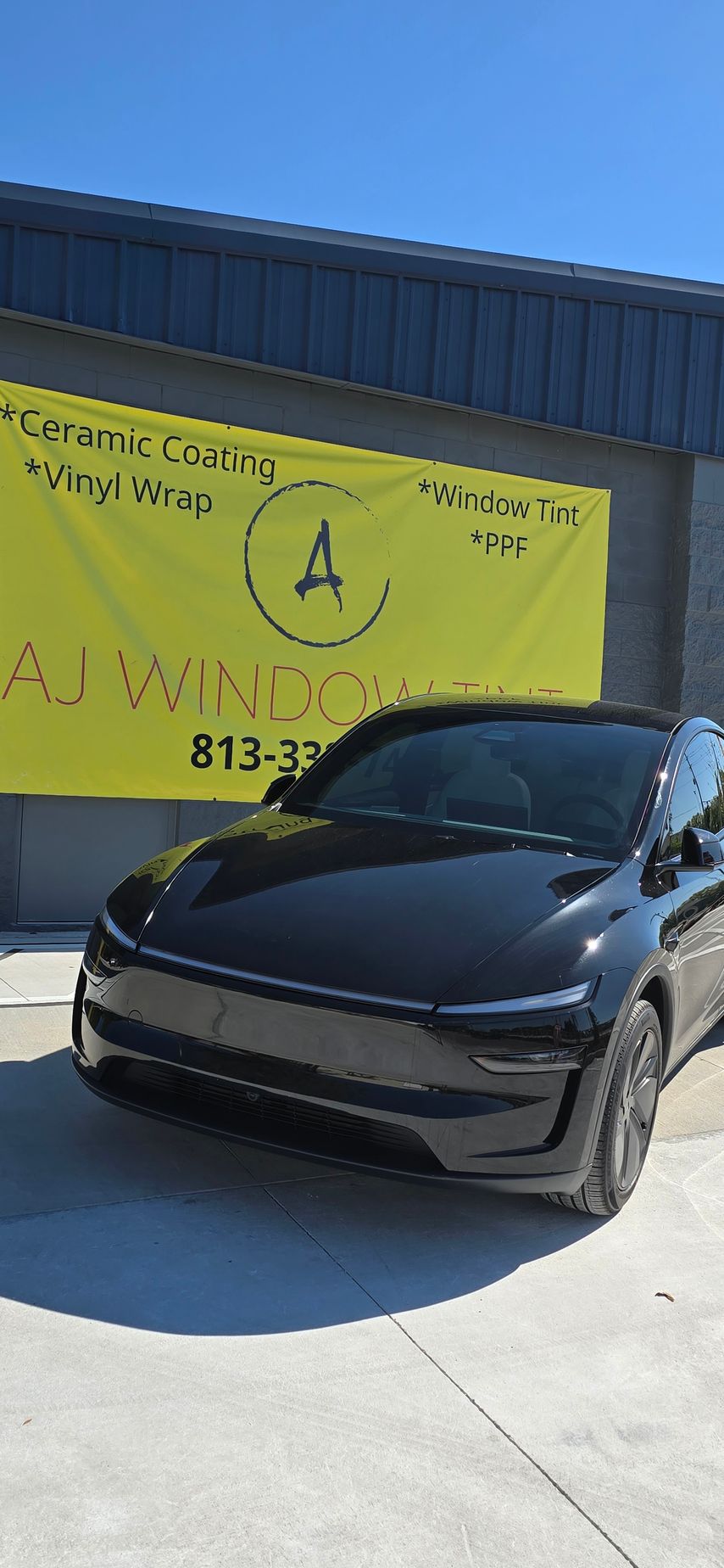 Black Tesla parked in front of a yellow AWNINGS storefront under a blue sky.