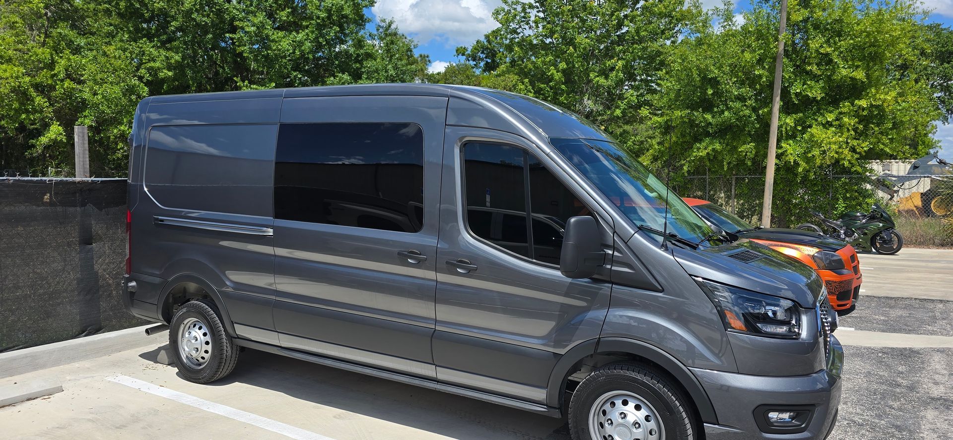 Black cargo van parked outdoors beside a stone wall and trees in daylight.