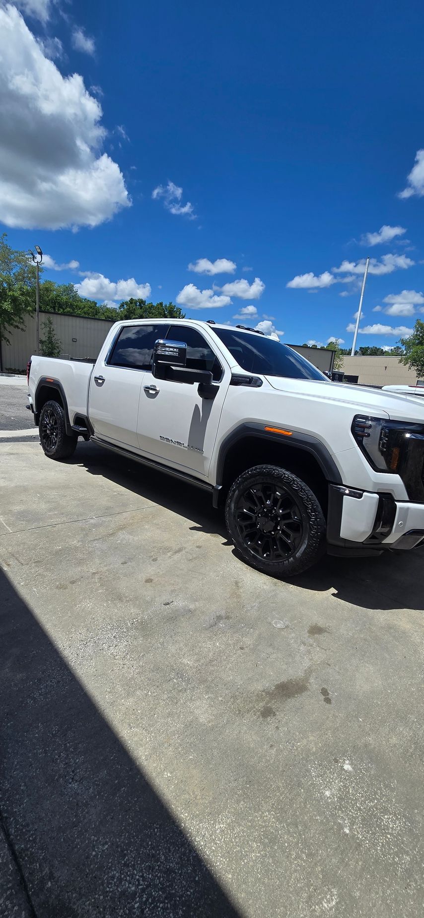 White lifted pickup truck parked on gravel under a bright blue sky with clouds