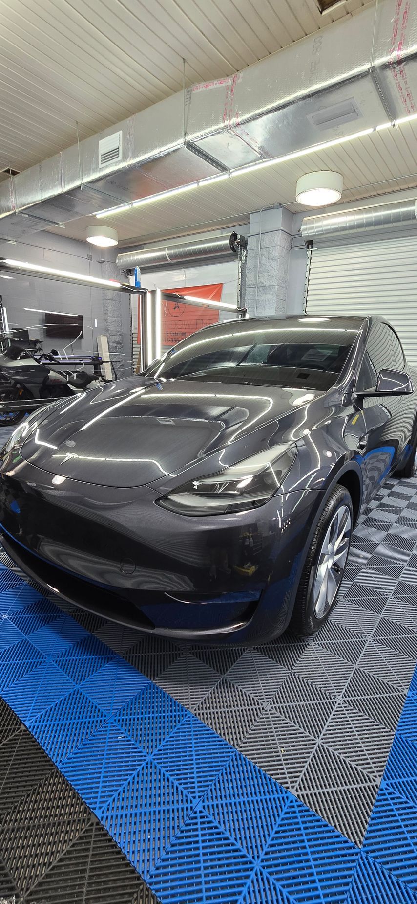 Black Tesla SUV in a garage-like shop with bright lights and blue floor mats.