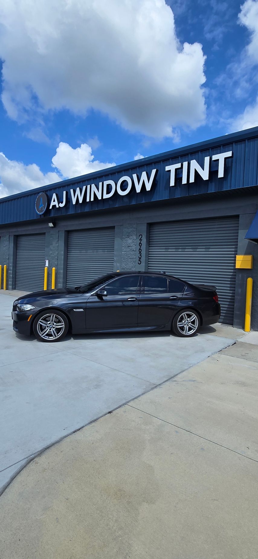 Black sedan parked outside AJ Window Tint shop under a cloudy sky