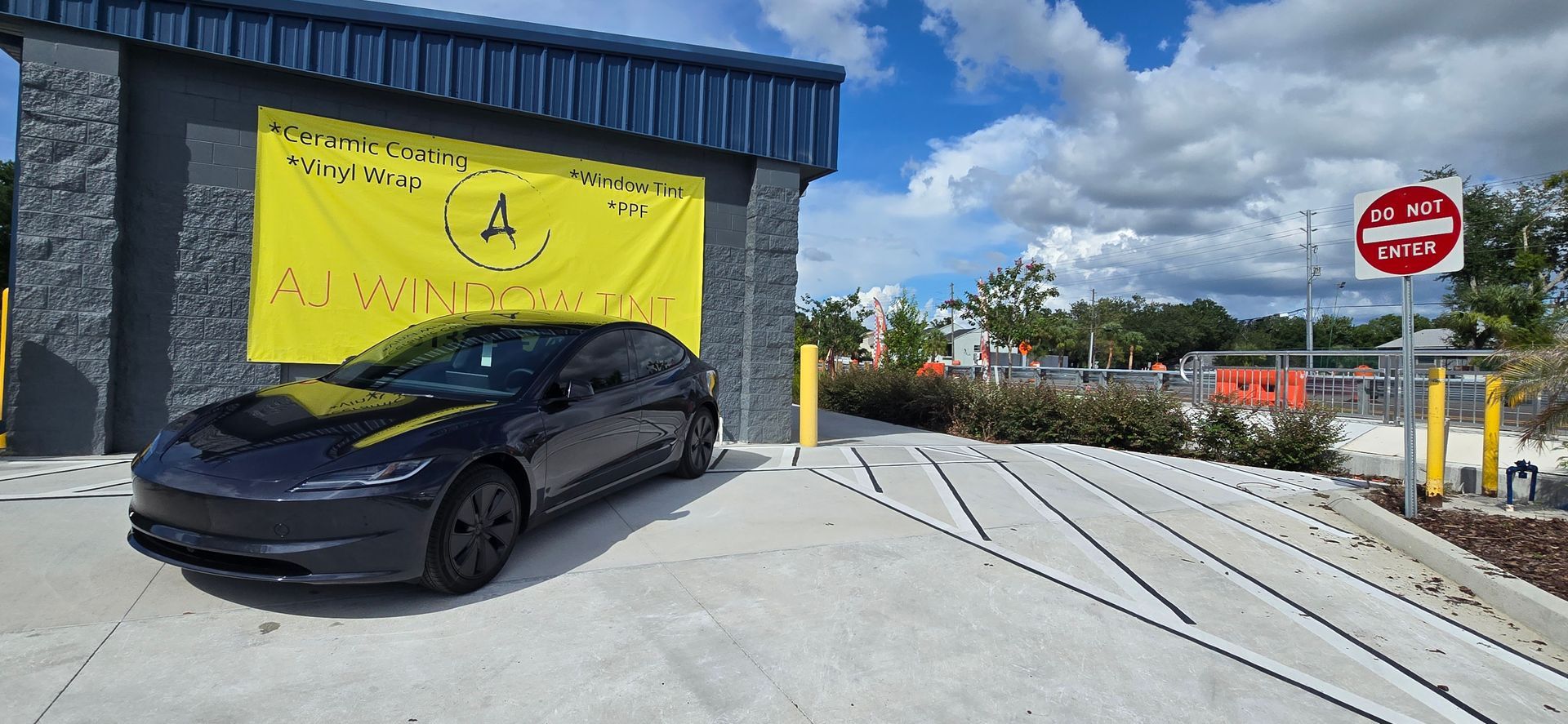 Black car parked beside a building with a yellow banner and a no entry sign near a sloped driveway