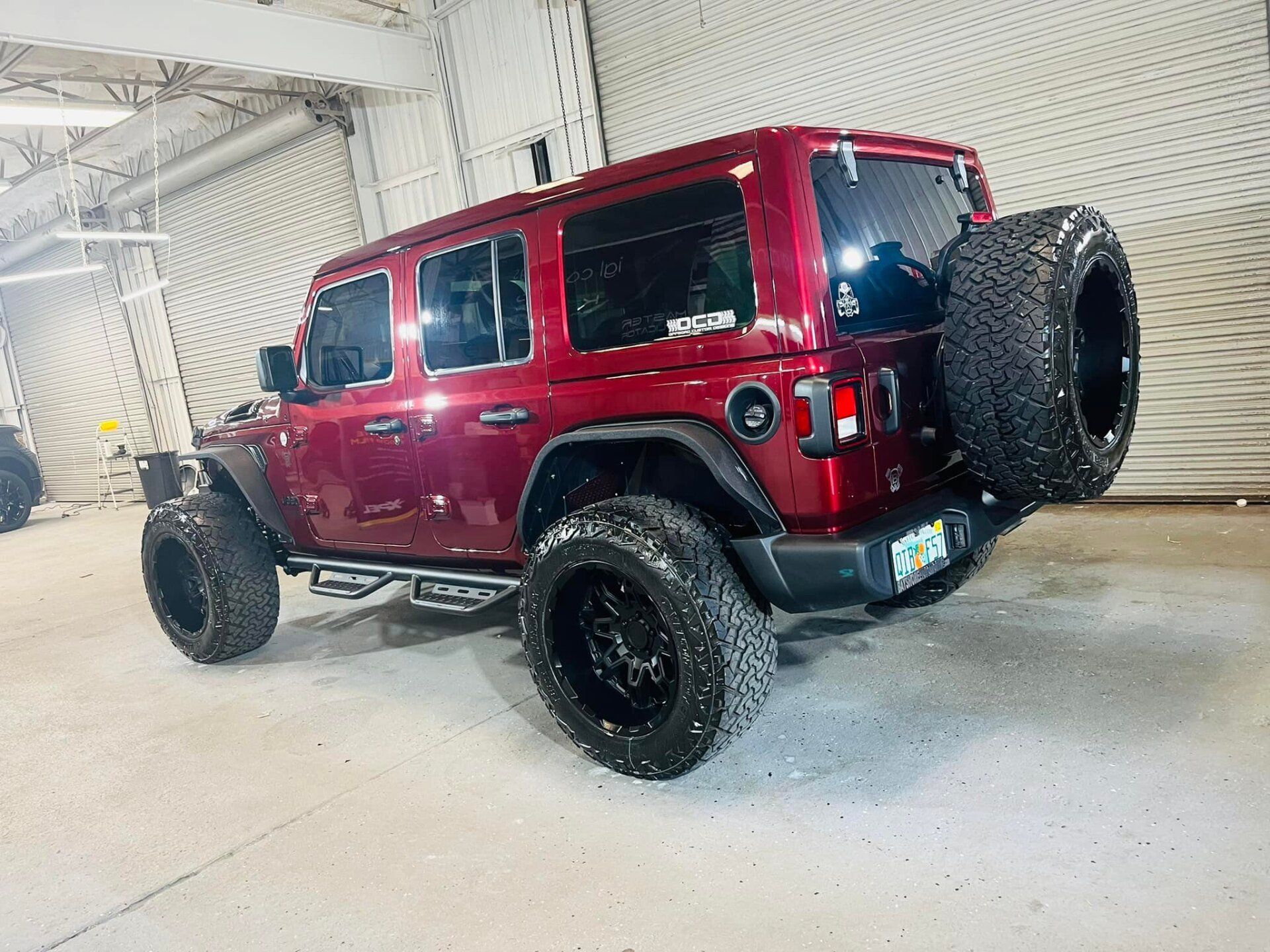 Red Jeep Wrangler with black wheels, spare tire, parked inside a building.