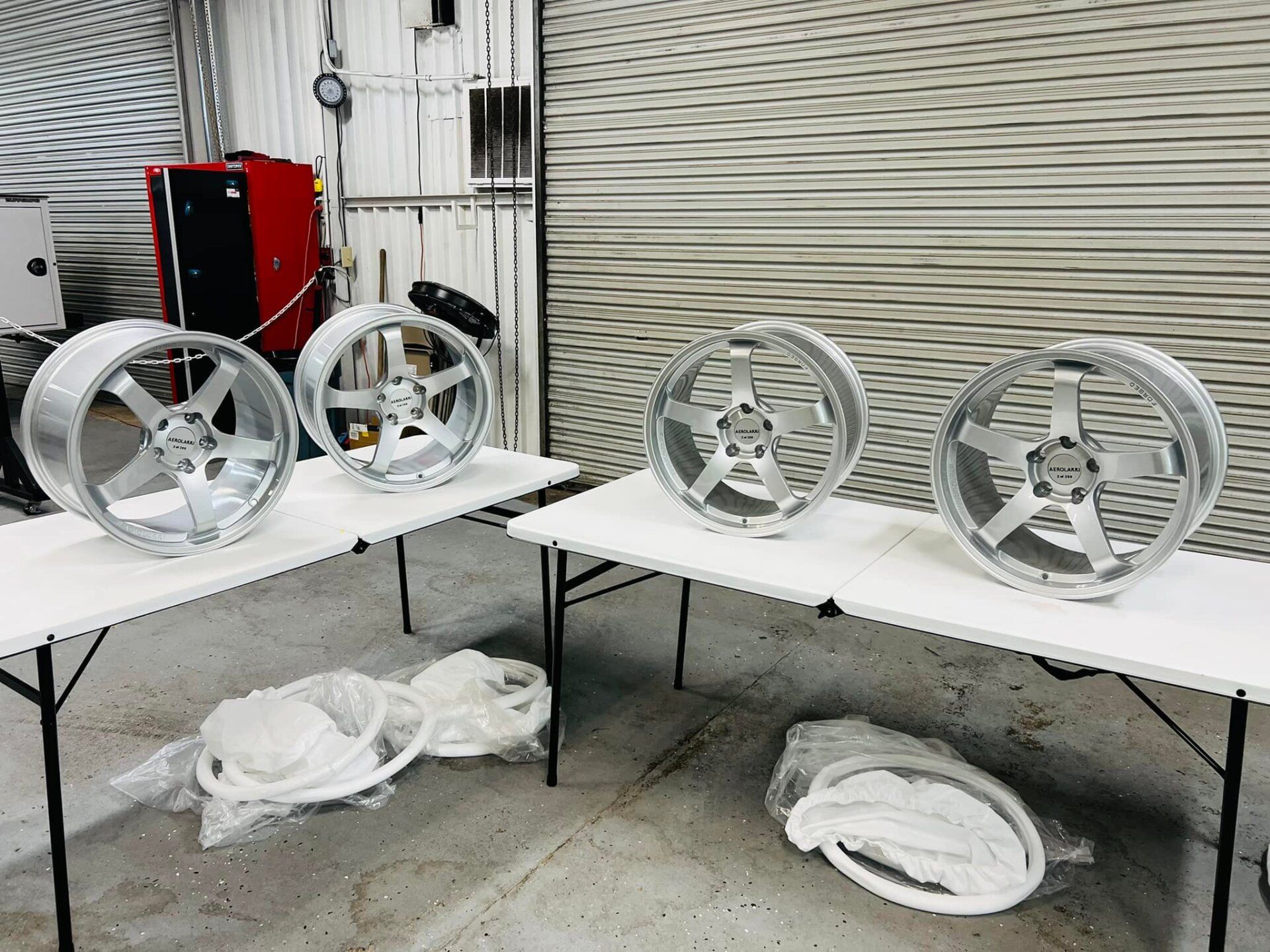 Four silver car rims displayed on folding tables in a shop setting.