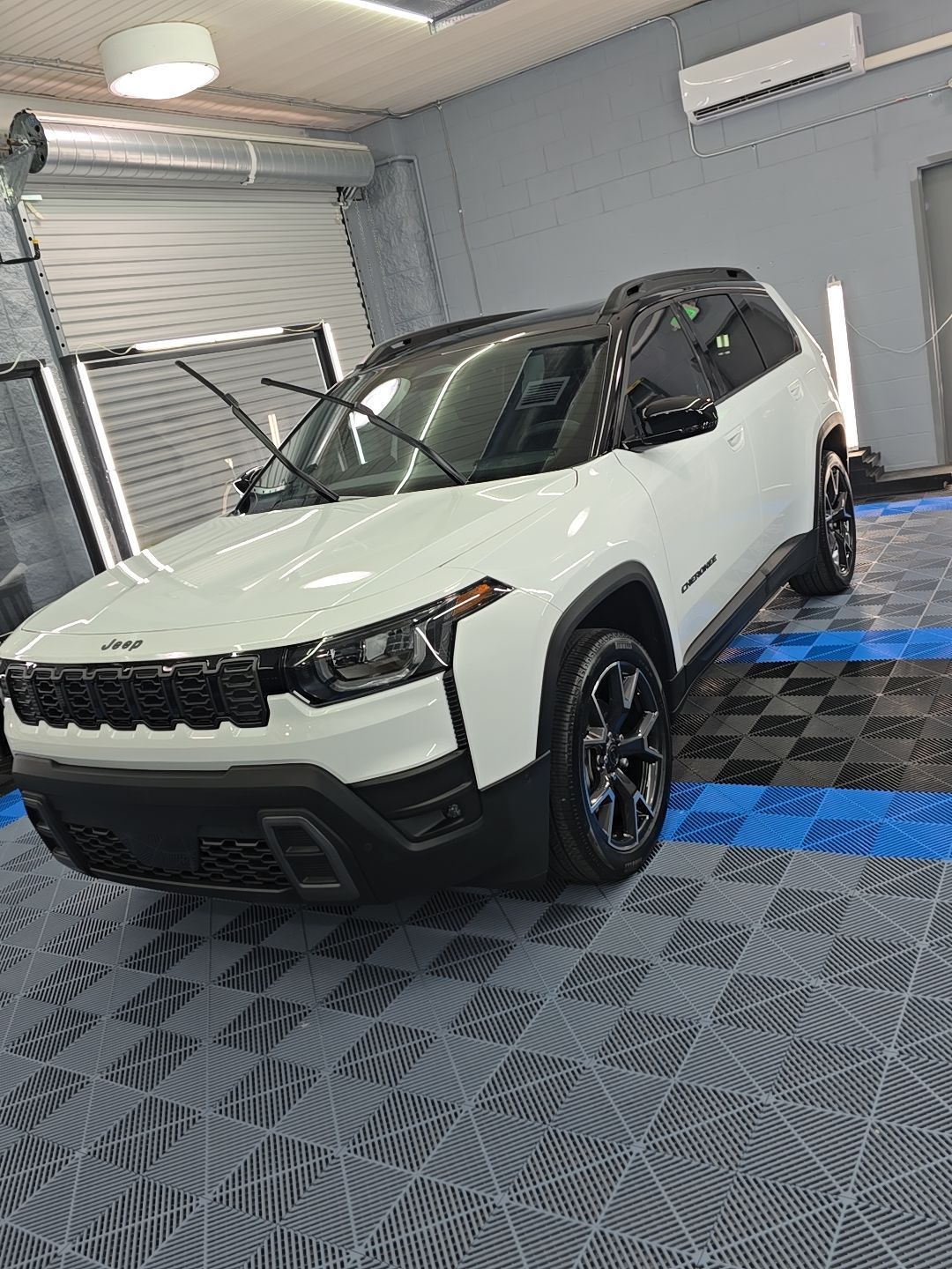White SUV with black roof parked indoors on a blue checkered floor in a garage.