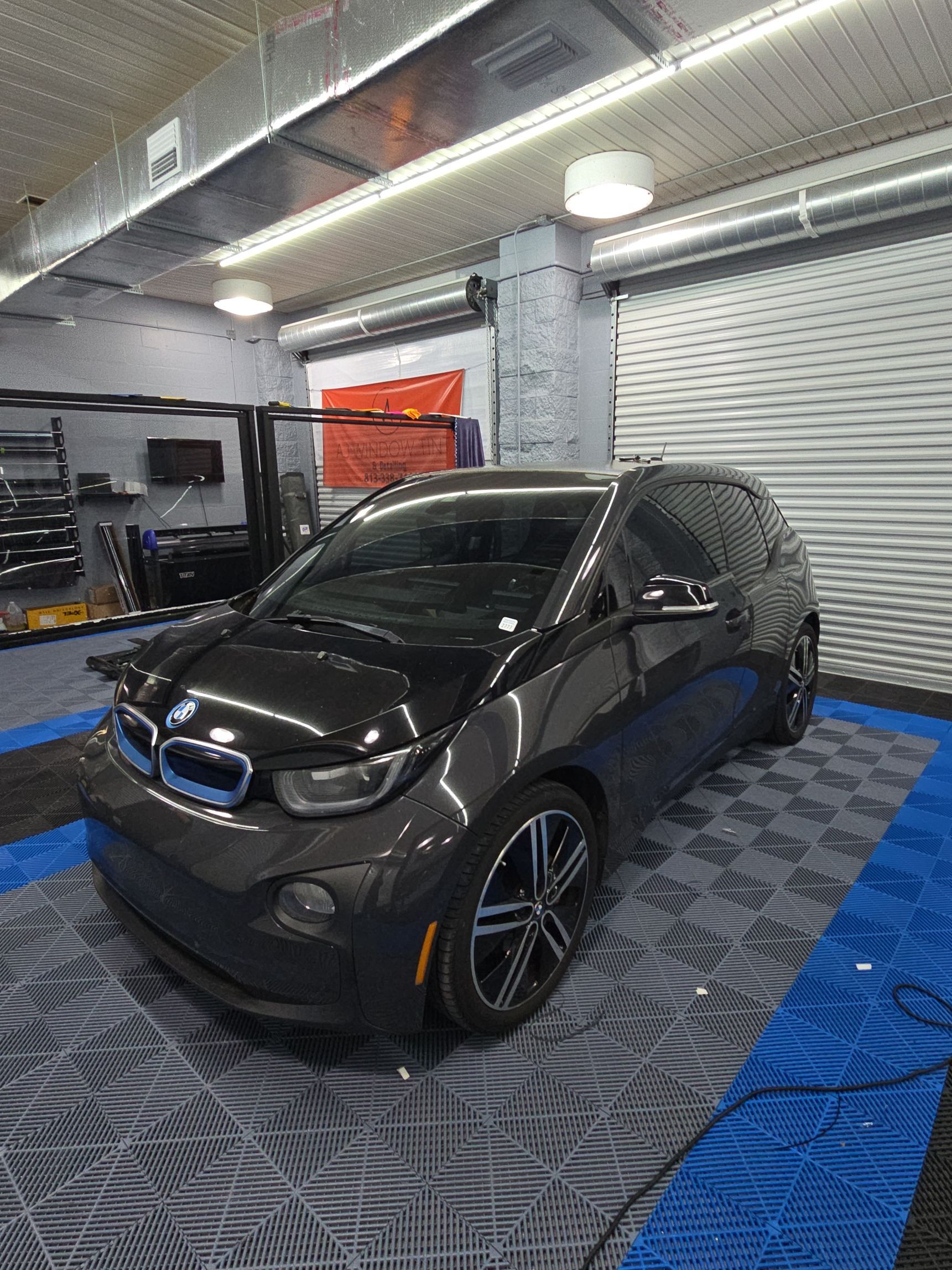 Black BMW i3 parked indoors on a blue patterned floor in a garage or detailing bay