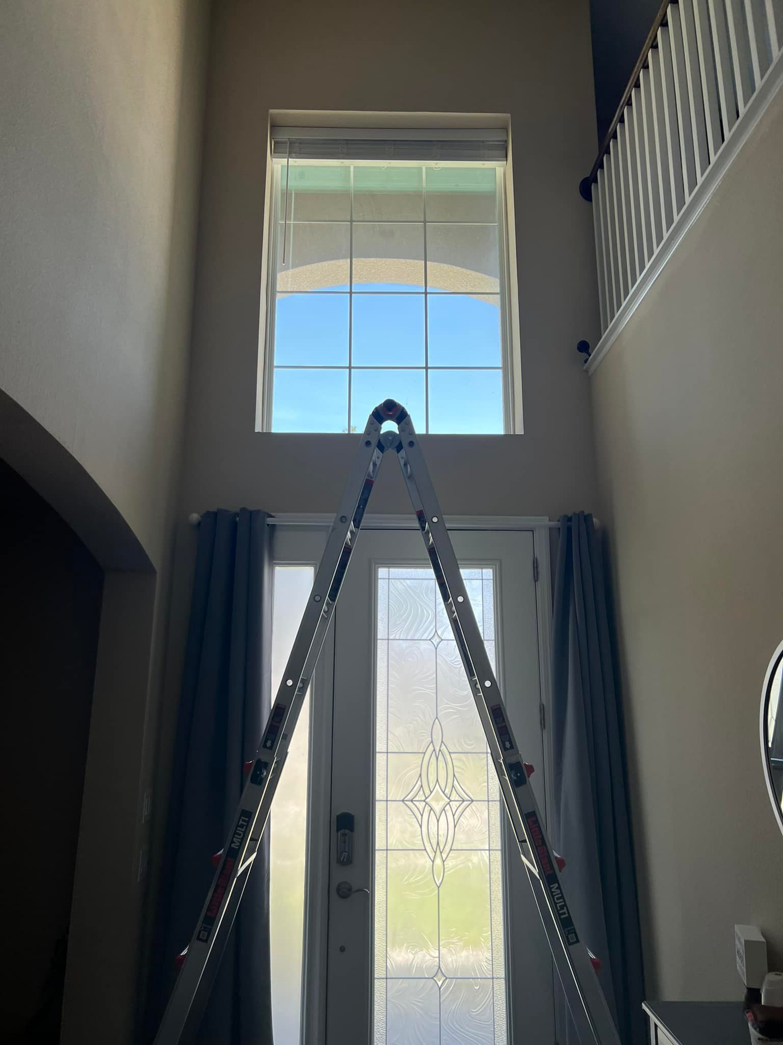 Ladder leaning against doors, reaching tall window. Curtains, foyer.