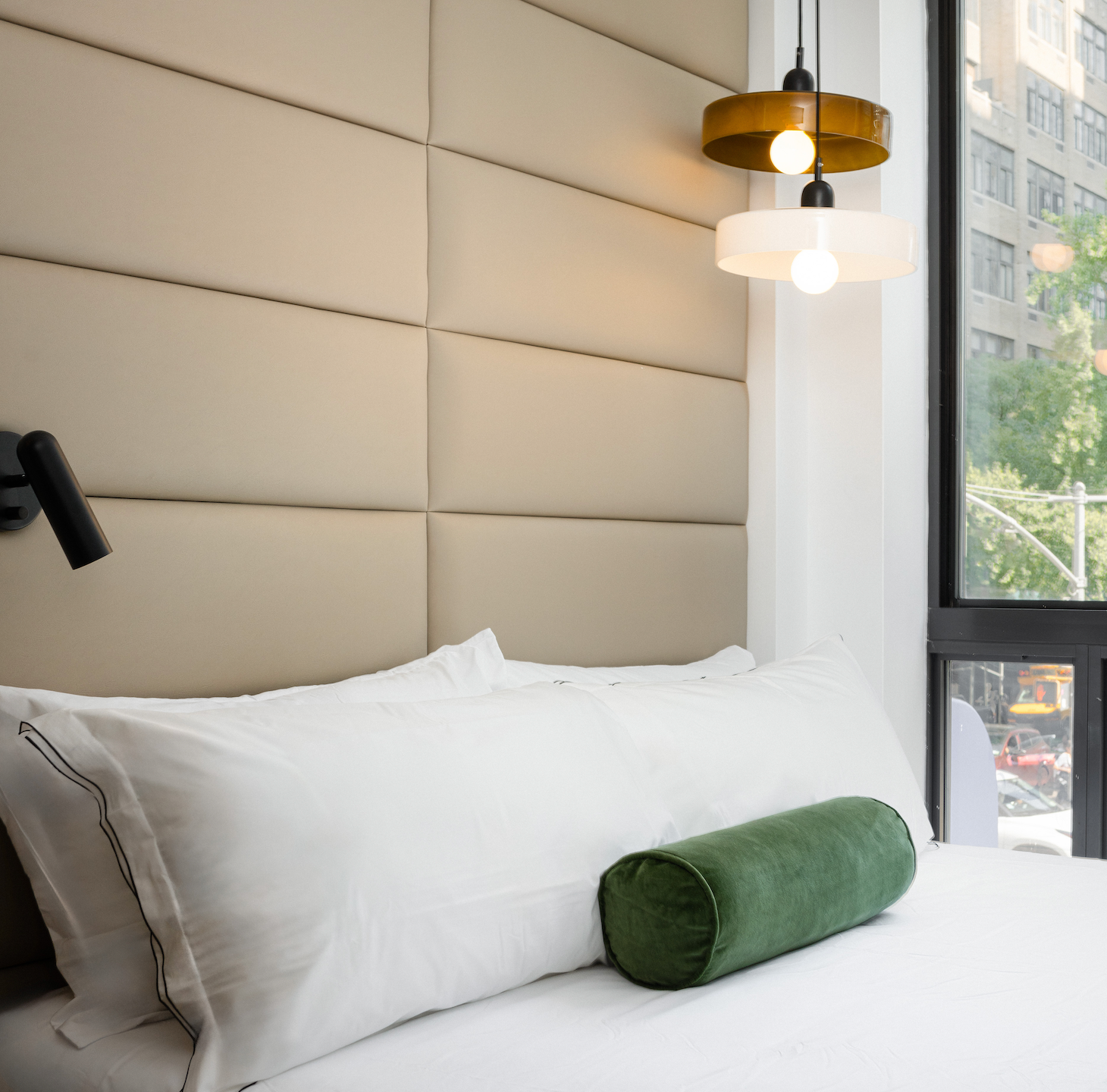 Bedroom with a bed, padded wall, hanging lights, and a window with a city view.