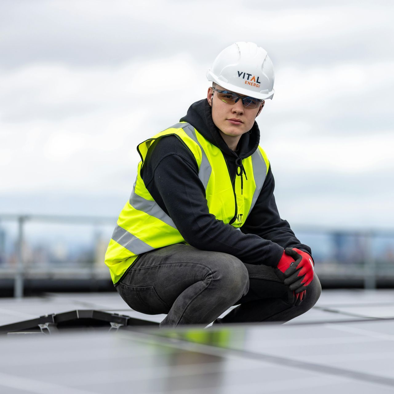 Construction worker in hard hat, safety vest inspecting solar panels on a rooftop.