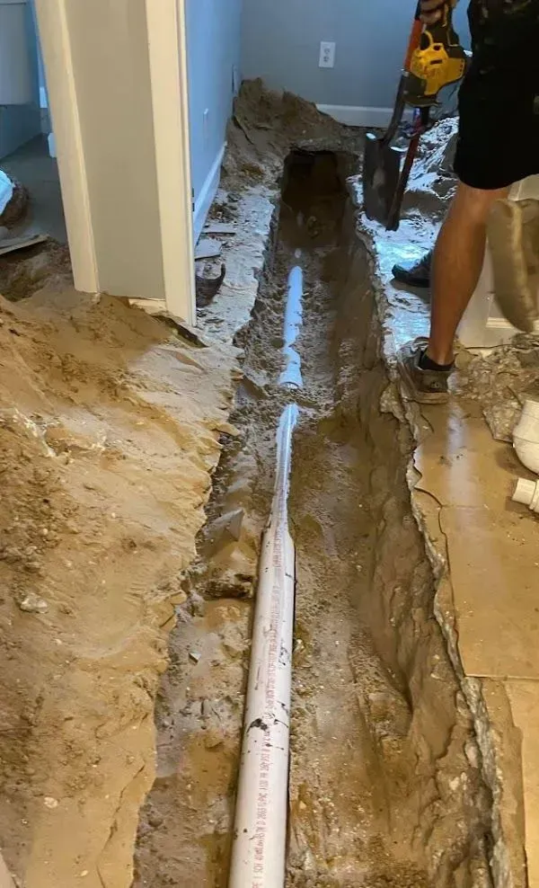 A trench dug for plumbing in a room. A person uses a jackhammer.