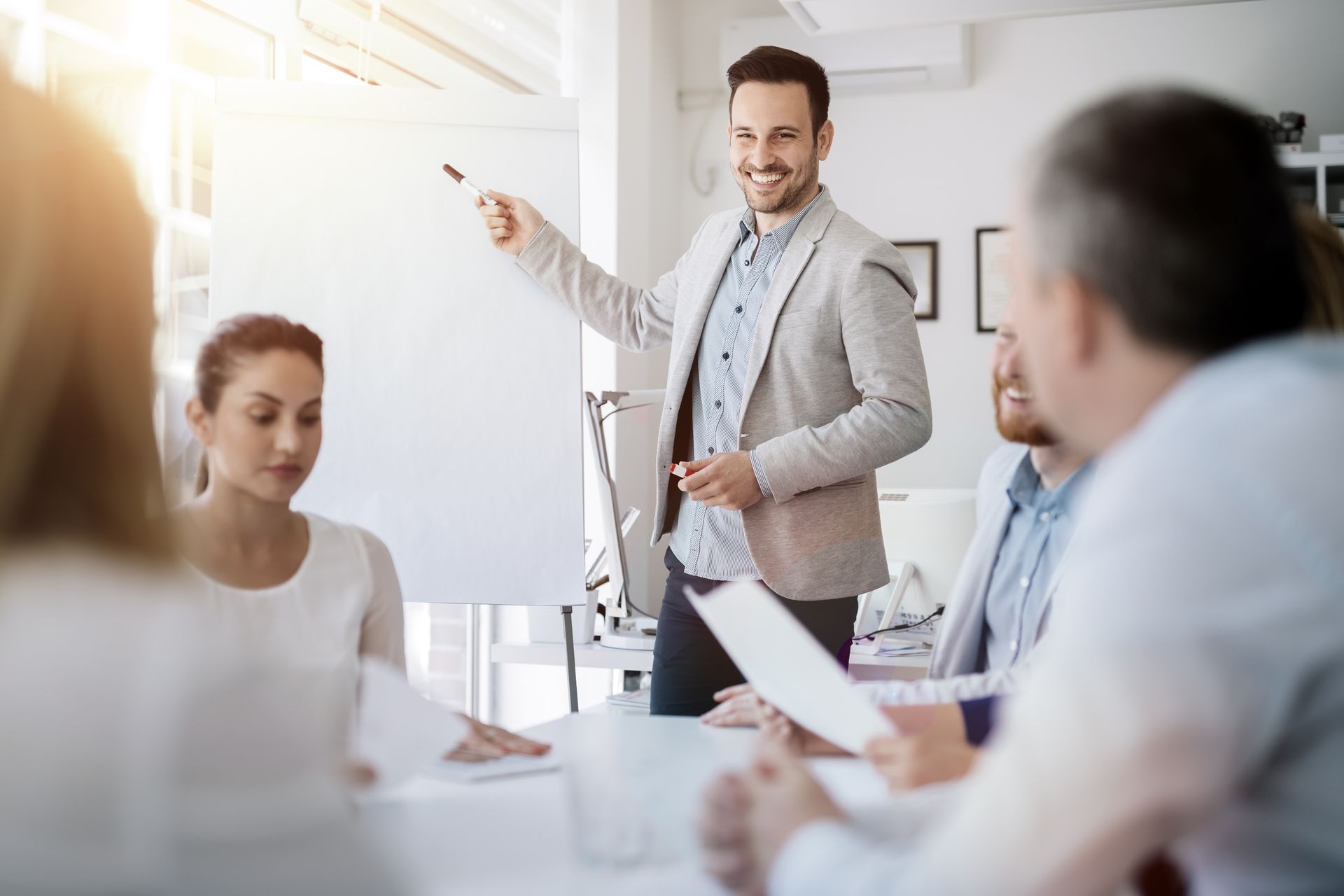 Man giving presentation to colleagues, pointing at whiteboard; office setting.