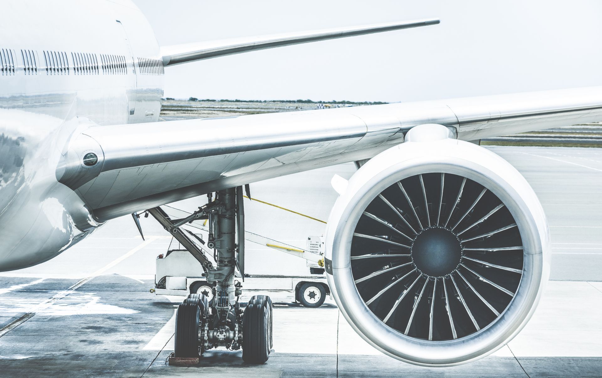 Close-up of an airplane engine and wing on the tarmac. Landing gear visible.