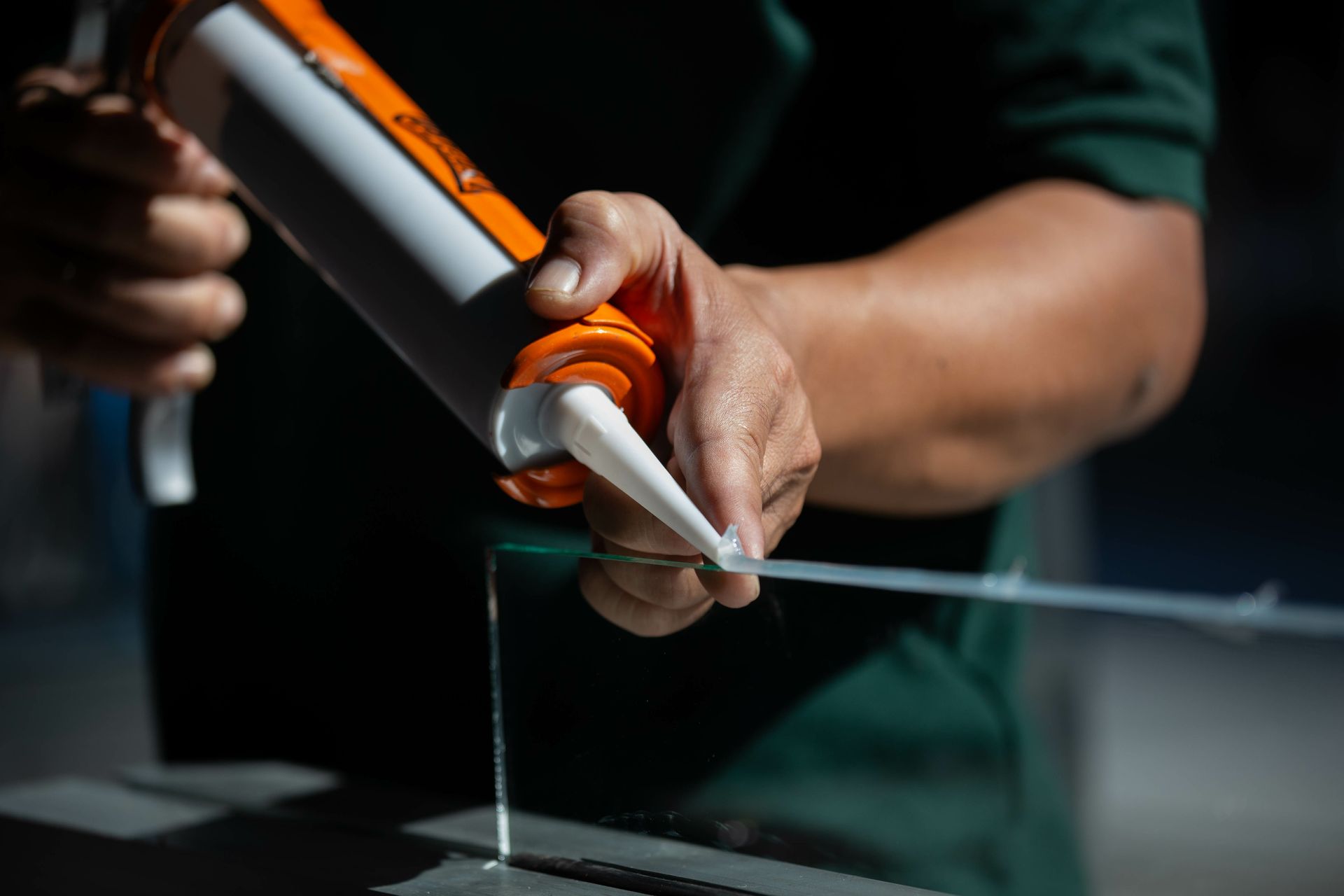 Person applying sealant to glass with an orange and white caulk gun.