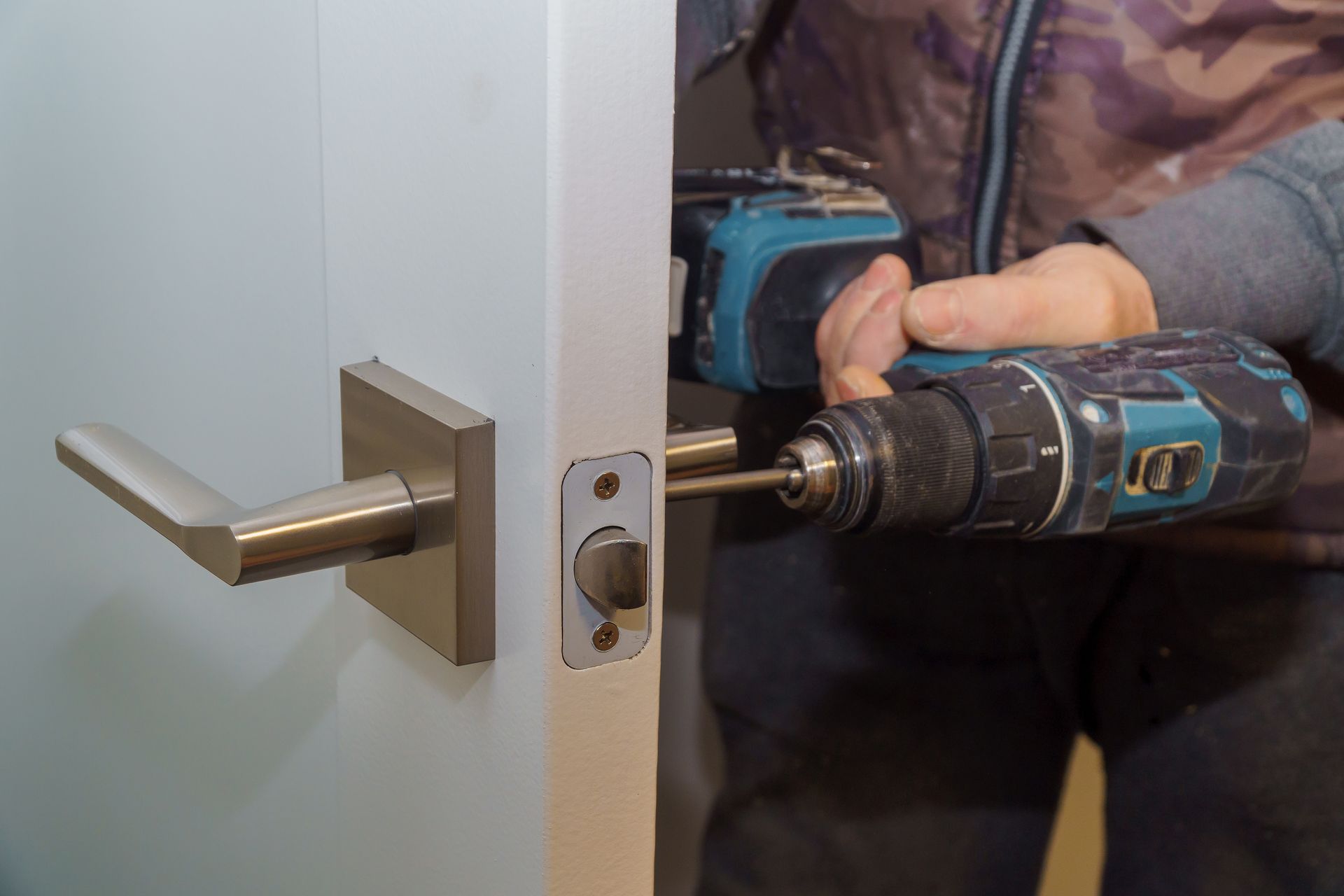 Person using a power drill to install a door handle on a white door.