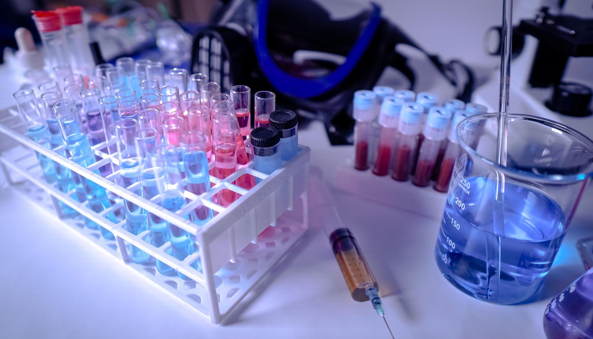 Laboratory setup with test tubes filled with colorful liquids, a beaker with blue liquid, and a syringe.