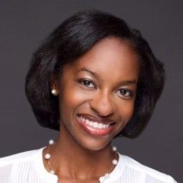 A woman wearing a white shirt and a pearl necklace is smiling.