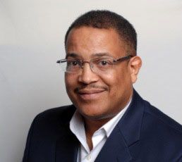 A man wearing glasses and a suit is smiling for the camera.