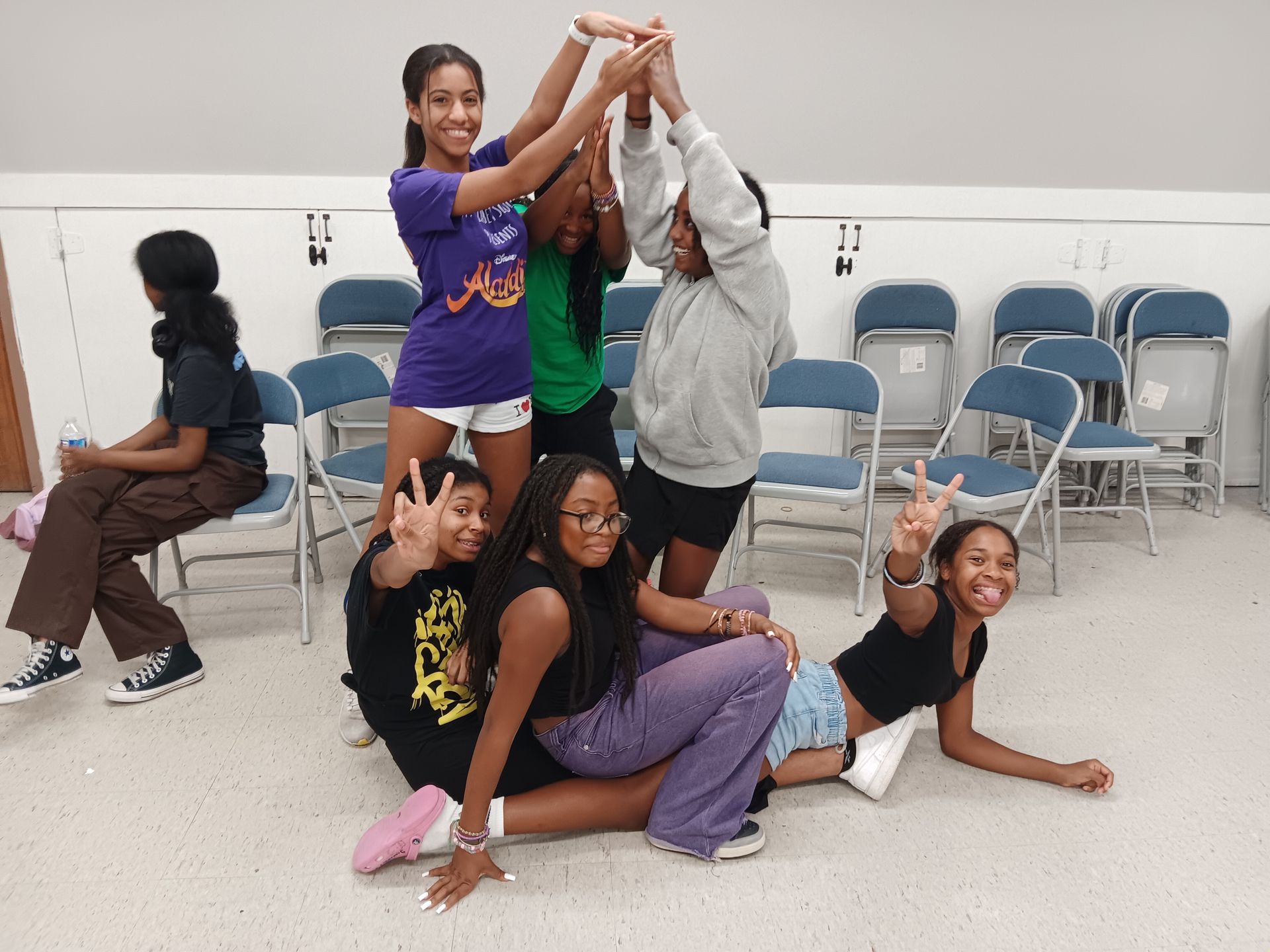 A group of young girls are posing for a picture in a room with folding chairs.