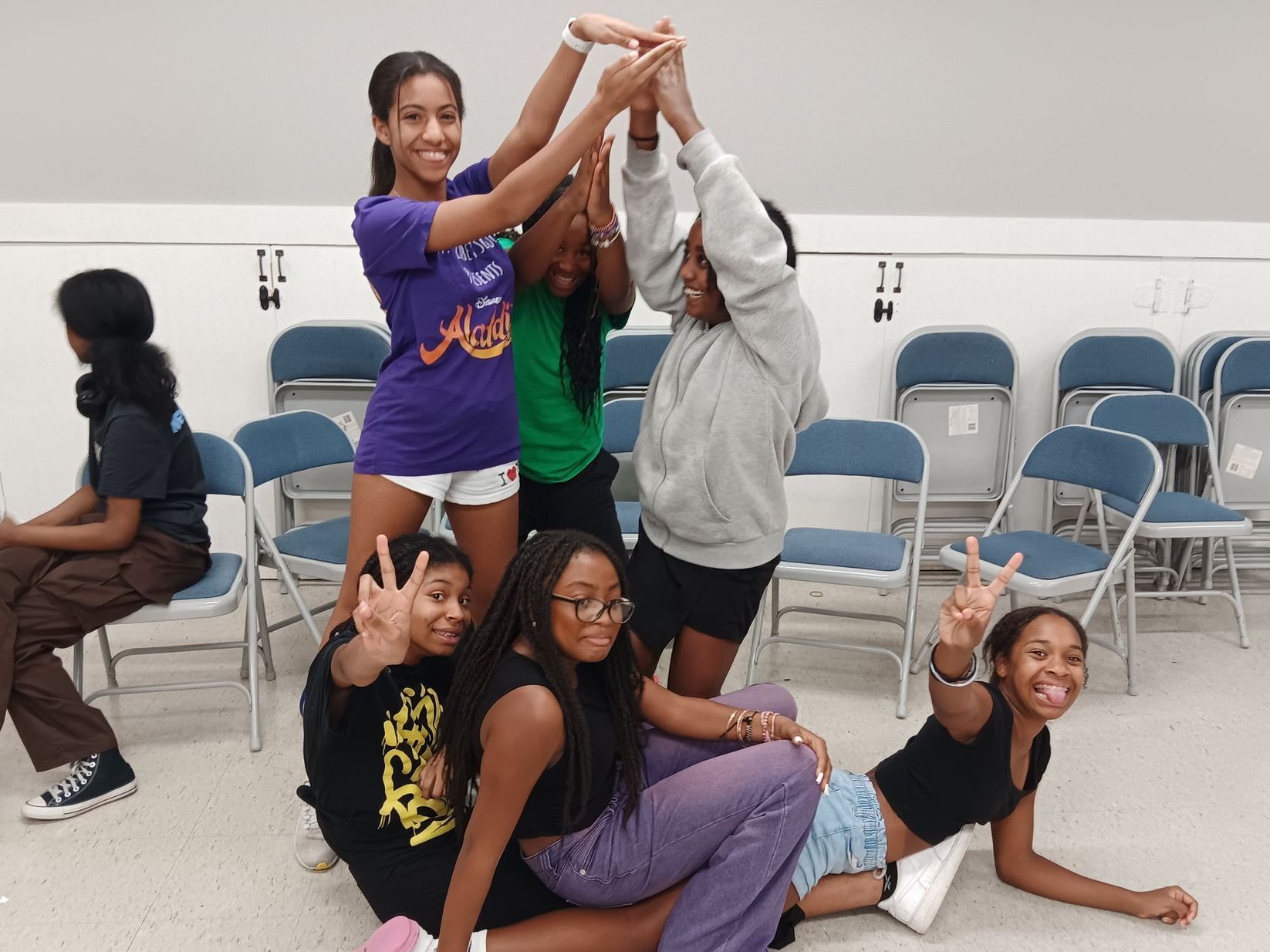 A group of young girls are posing for a picture in a room with folding chairs.