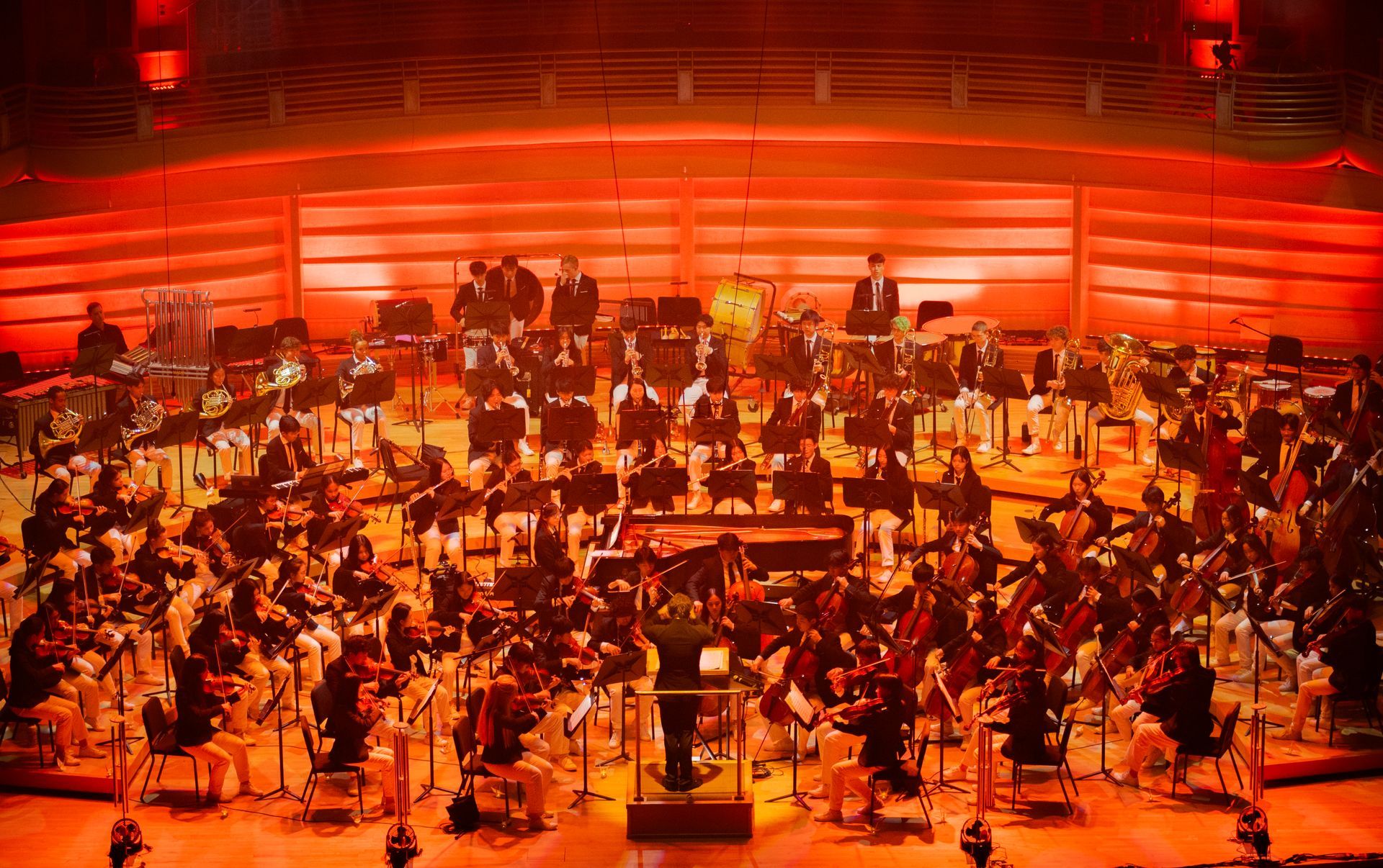 A large orchestra is playing on a stage with red lights.
