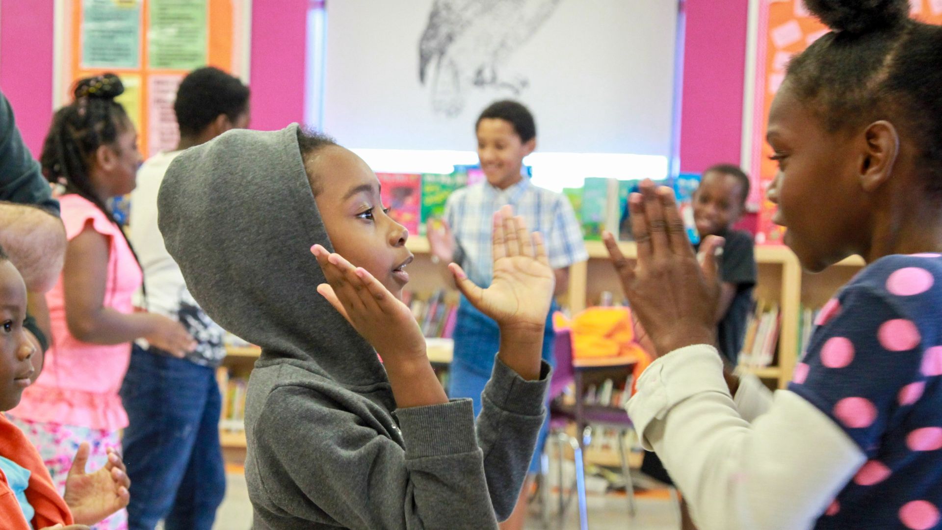 A group of children are clapping their hands in a classroom.