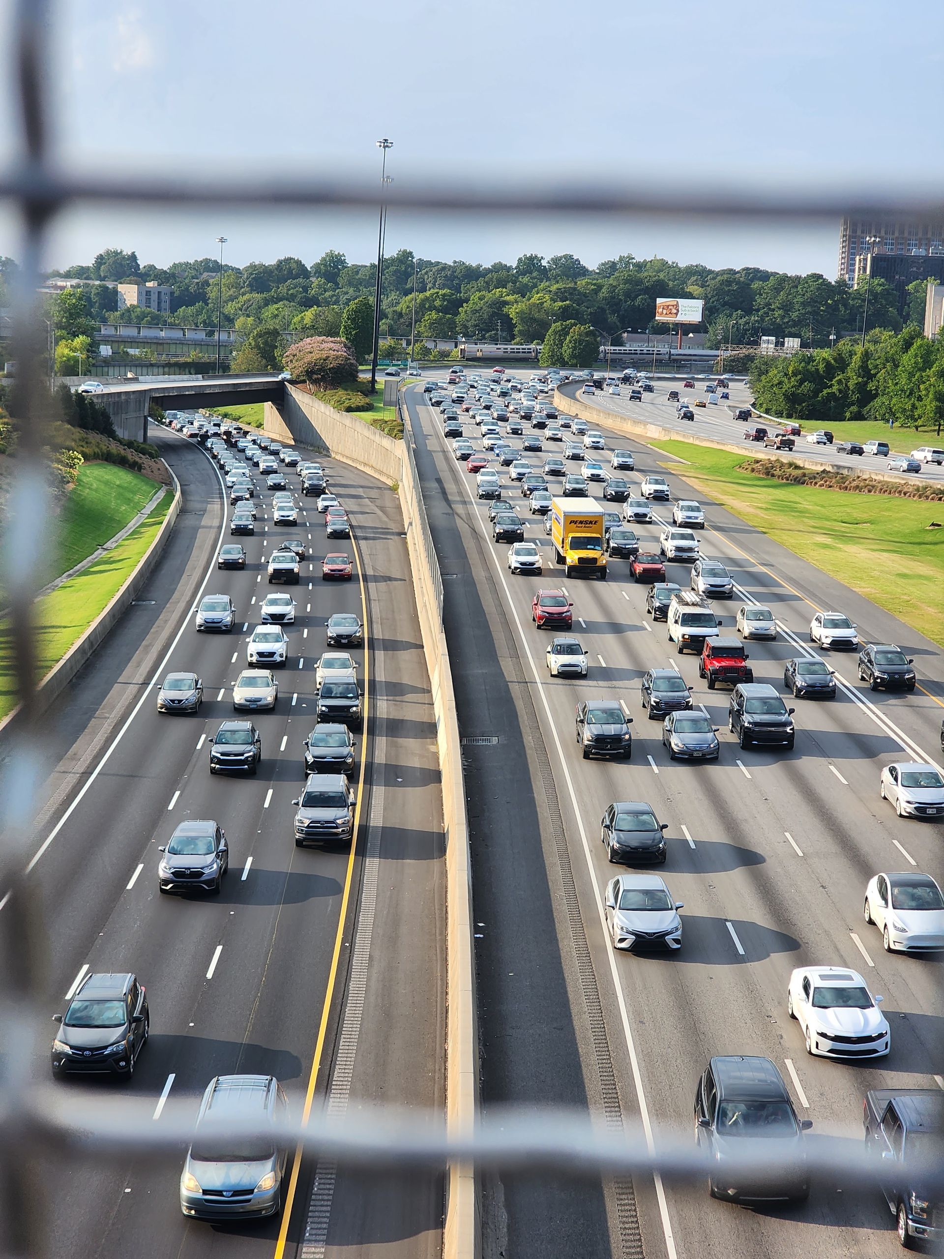 Cars in heavy traffic on multi-lane highway, viewed from above, framed by a metal railing.
