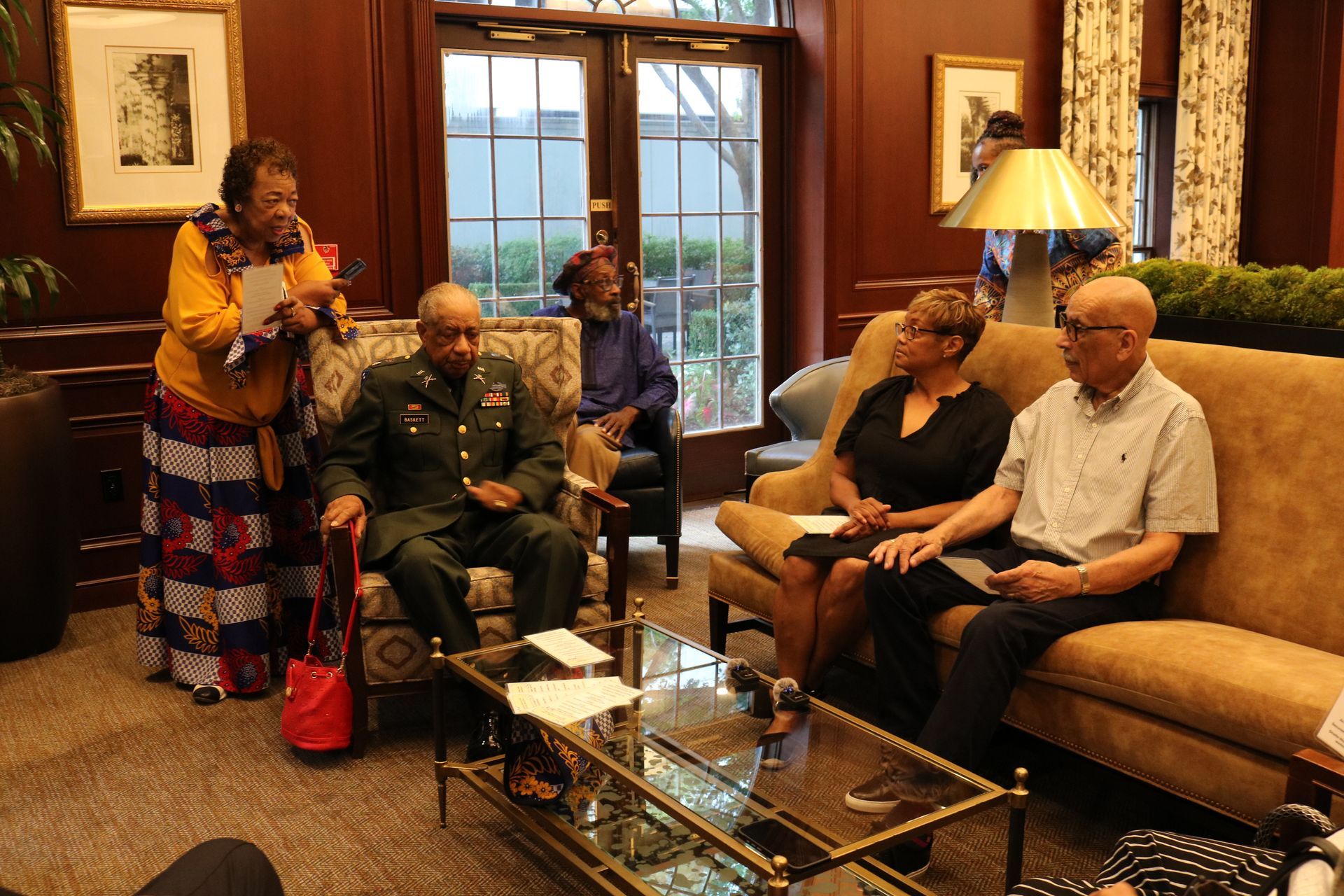Group of people in a room, some seated, with a woman speaking.