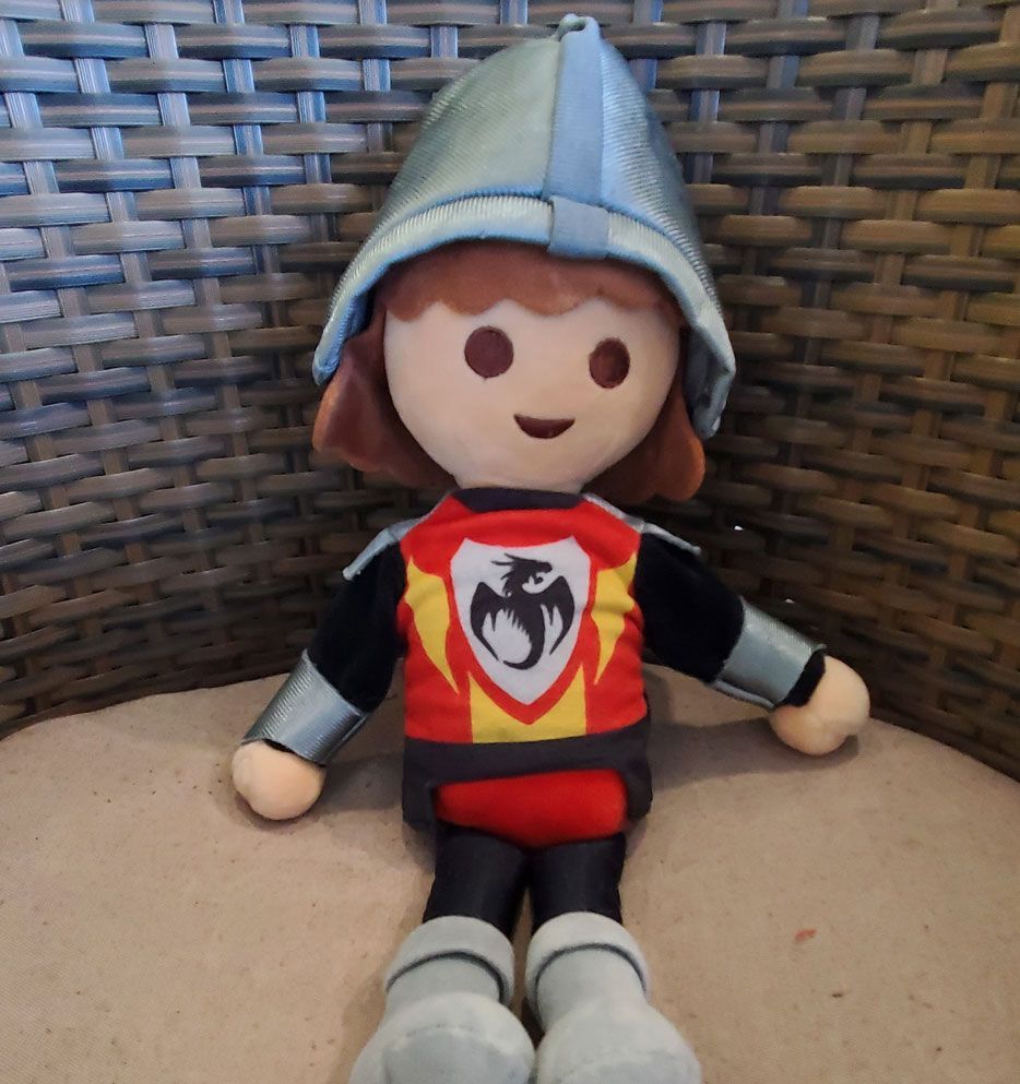 Plüschtier eines Ritters mit rot-gelbem Schild und blauem Helm, der auf einem Korbstuhl sitzt.