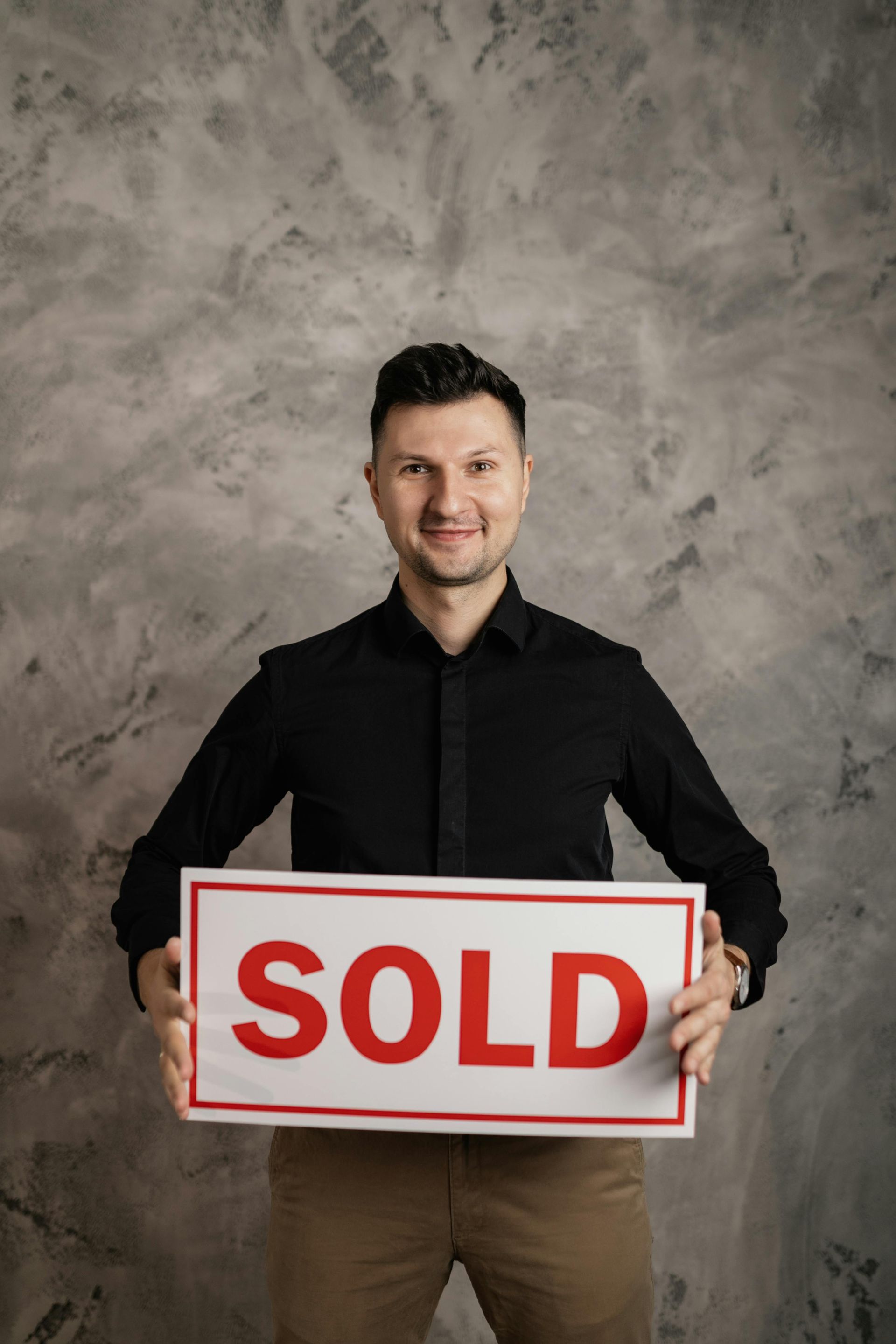 A man is holding a sold sign in his hands.