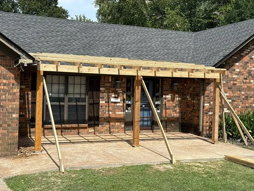 Construction of a wooden porch roof attached to a brick home with supporting beams and braces.