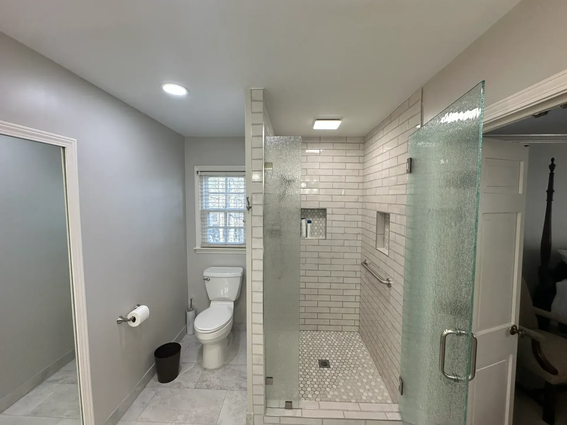 Bathroom with white and gray tile, toilet, and a glass shower with decorative glass.