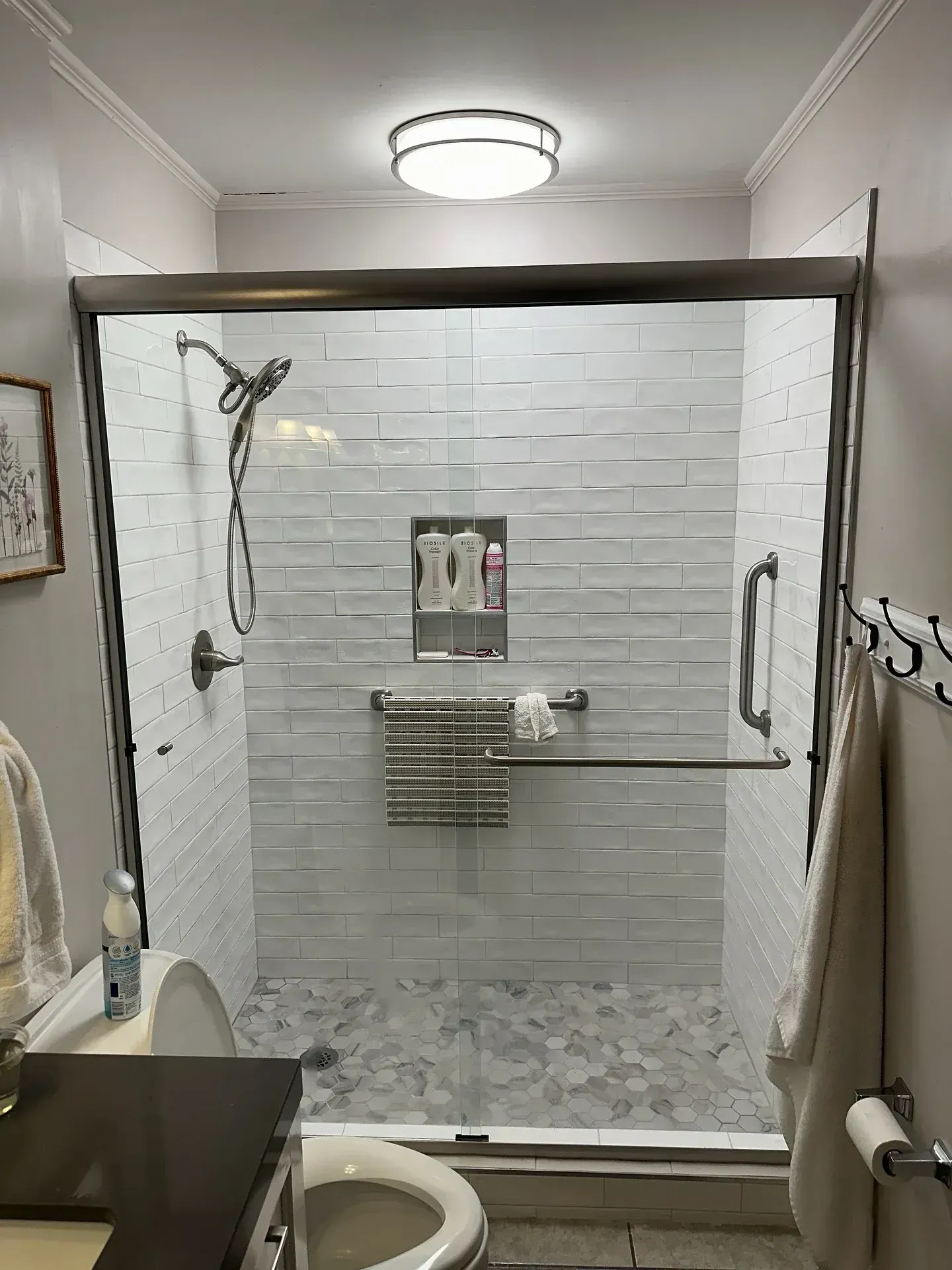 Bathroom with white textured tile shower, glass door, and gray stone floor. Includes toilet and sink.
