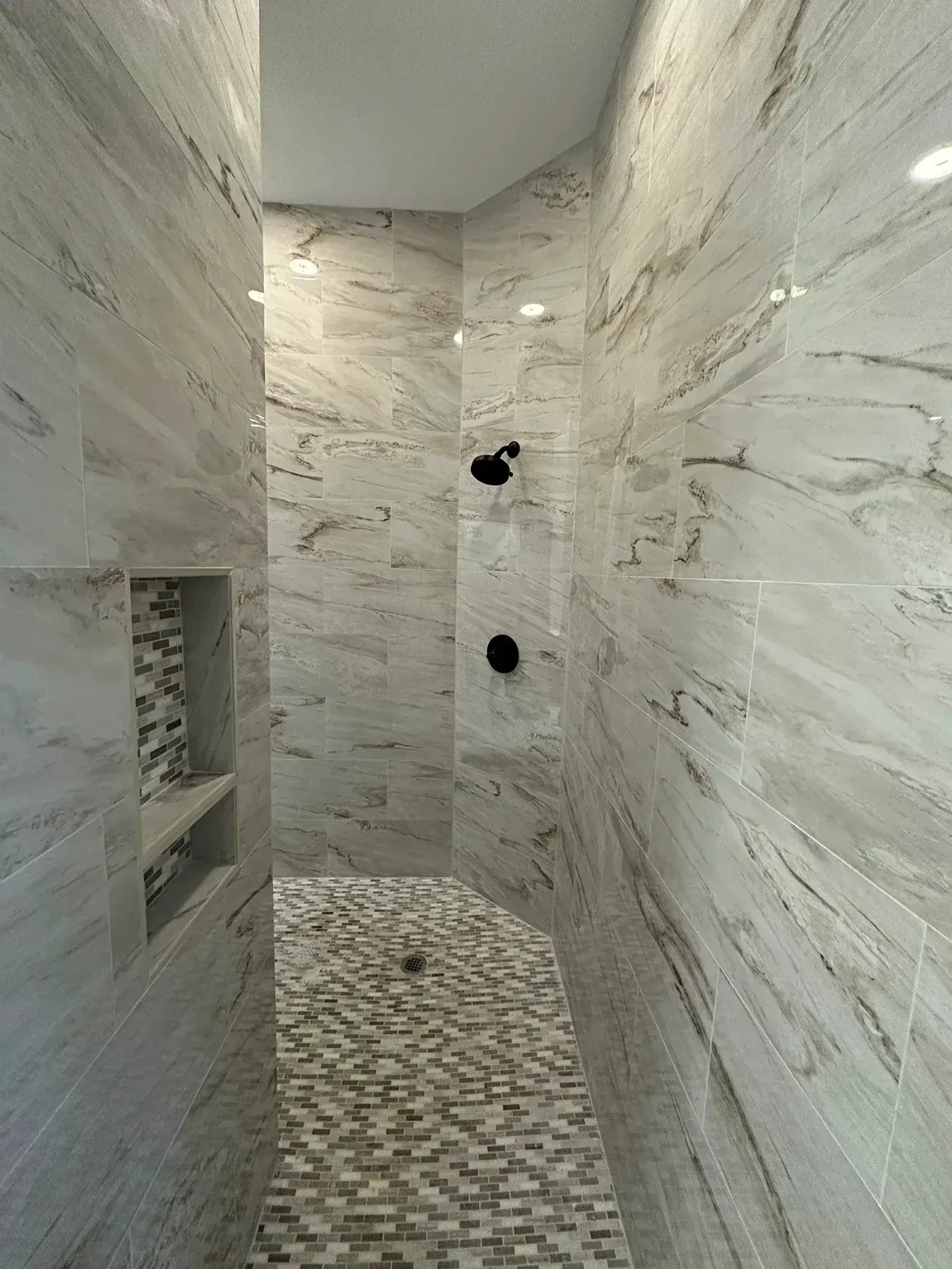 Modern shower with stone tile walls, pebble floor, and black shower fixtures.