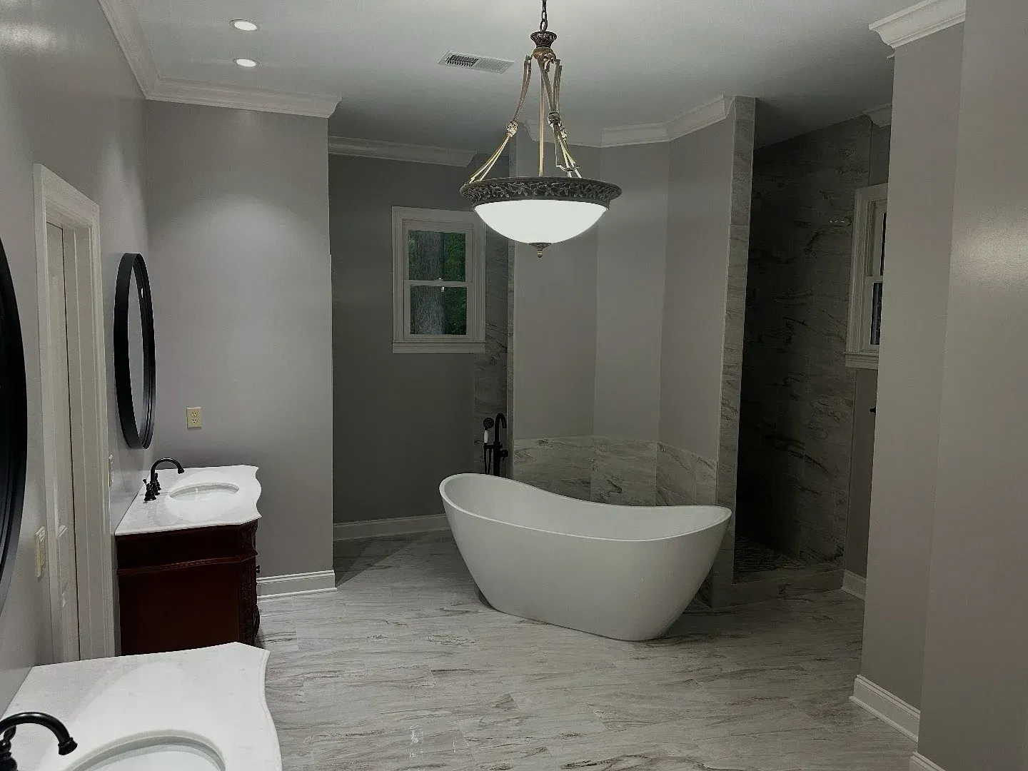 Gray and white bathroom with a freestanding tub, dual vanities, and a hanging light.