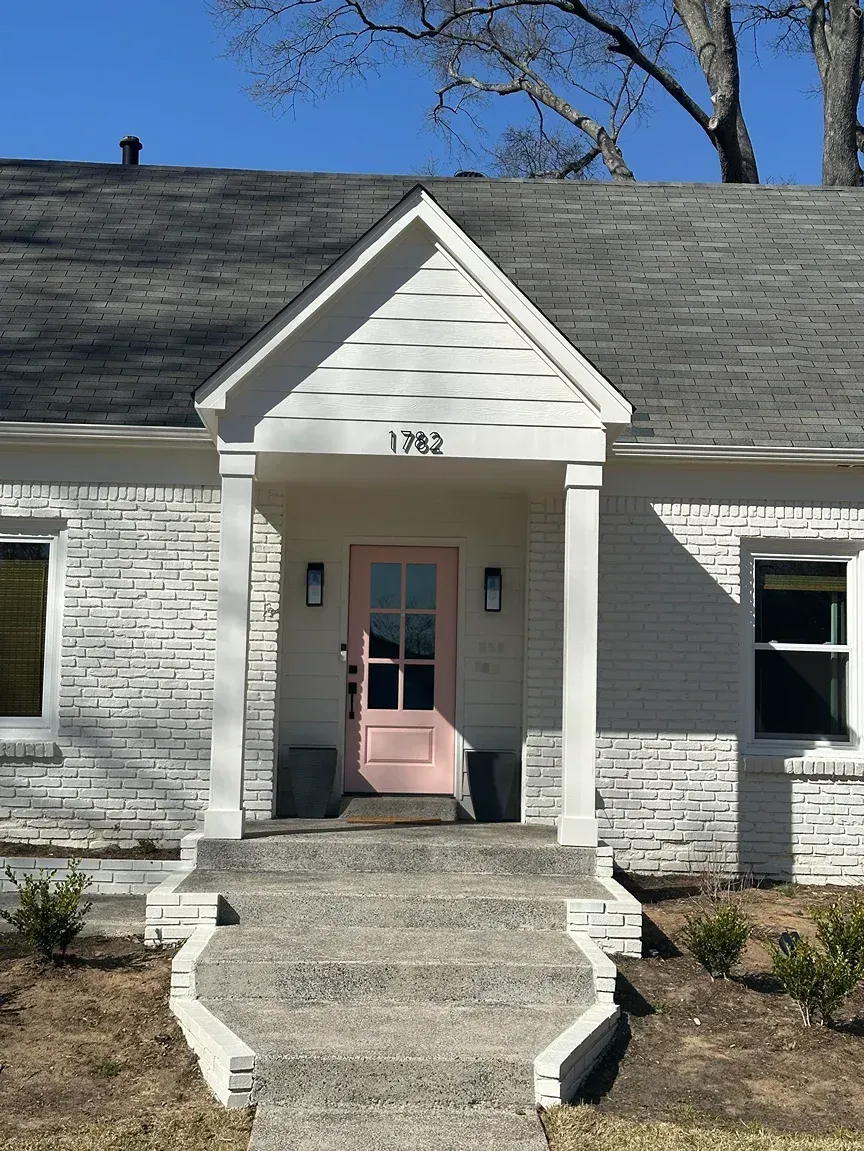 Pink front door of a white-painted brick house with a small porch, steps, and two planters.