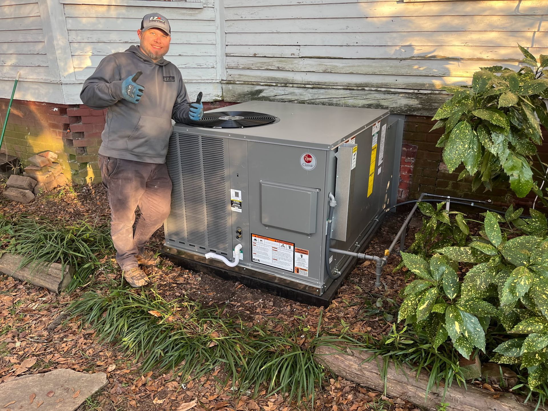 A man gives a thumbs up next to a newly installed air conditioning unit outside a house with peeling paint.