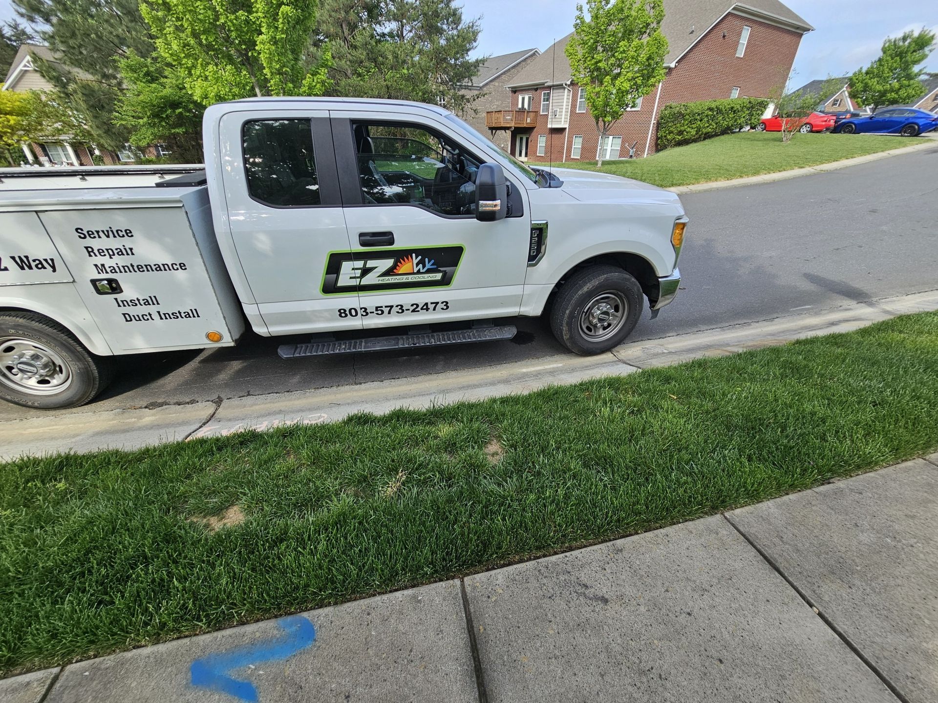 A white EZEI landscaping truck parked on the side of a street next to a green lawn.