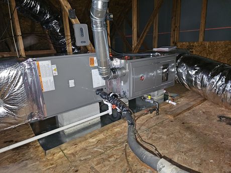 HVAC unit installed in an attic. Ductwork is connected. The unit is metallic, and the attic has wood framing.