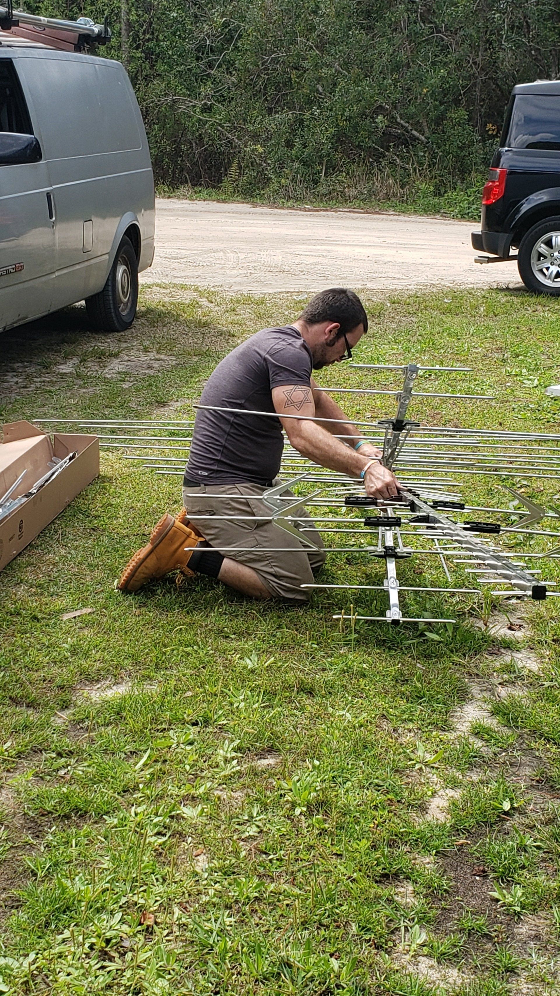 A man is kneeling down in the grass working on an antenna.