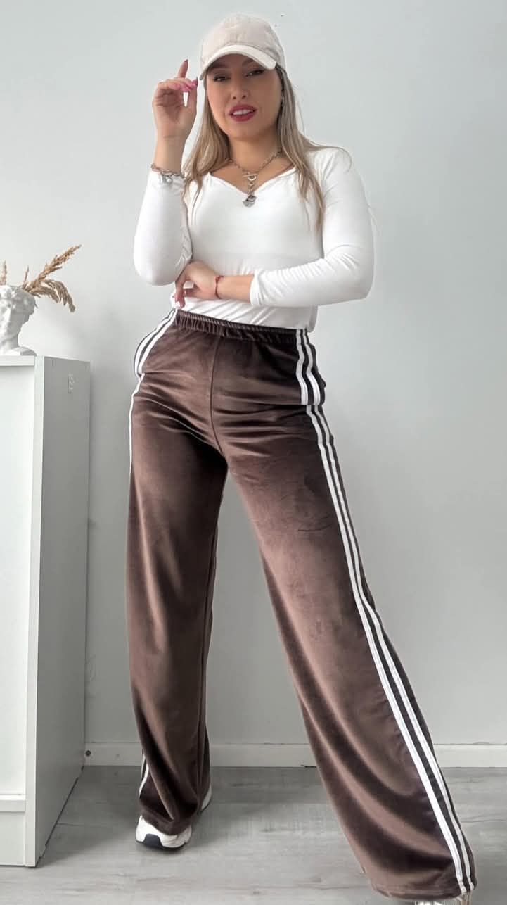 La mujer lleva una camisa blanca y pantalones marrones con rayas blancas en los costados.