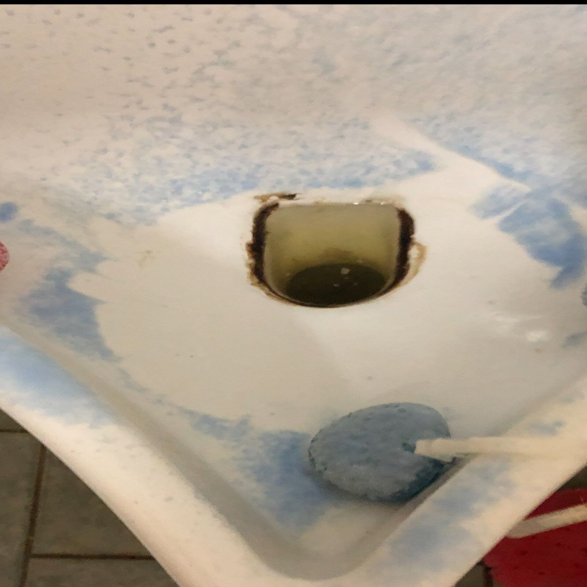 Close-up of a dirty sink drain. Blue residue surrounds the drain hole. A sponge is in the corner.