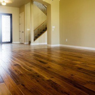 Wooden floor in an empty room with a staircase, beige walls, and a door with sunlight.