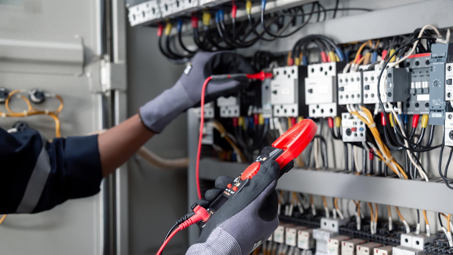 An electrician is working on an electrical panel with a multimeter.