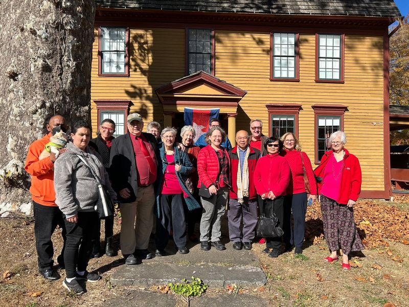 Group of People in Red Stand in Front of A Yellow House with A Brown Roof — Amherst, MA — Immanuel Lutheran Church