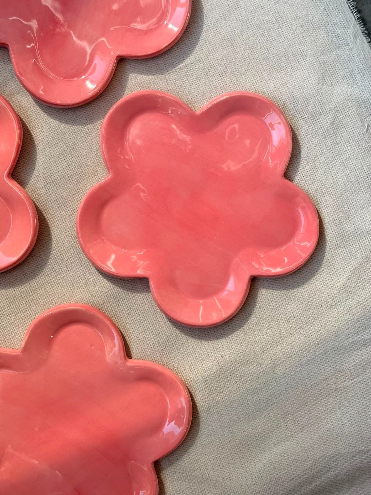 Platos de cerámica rosa con forma de flor sobre un fondo de tela clara.