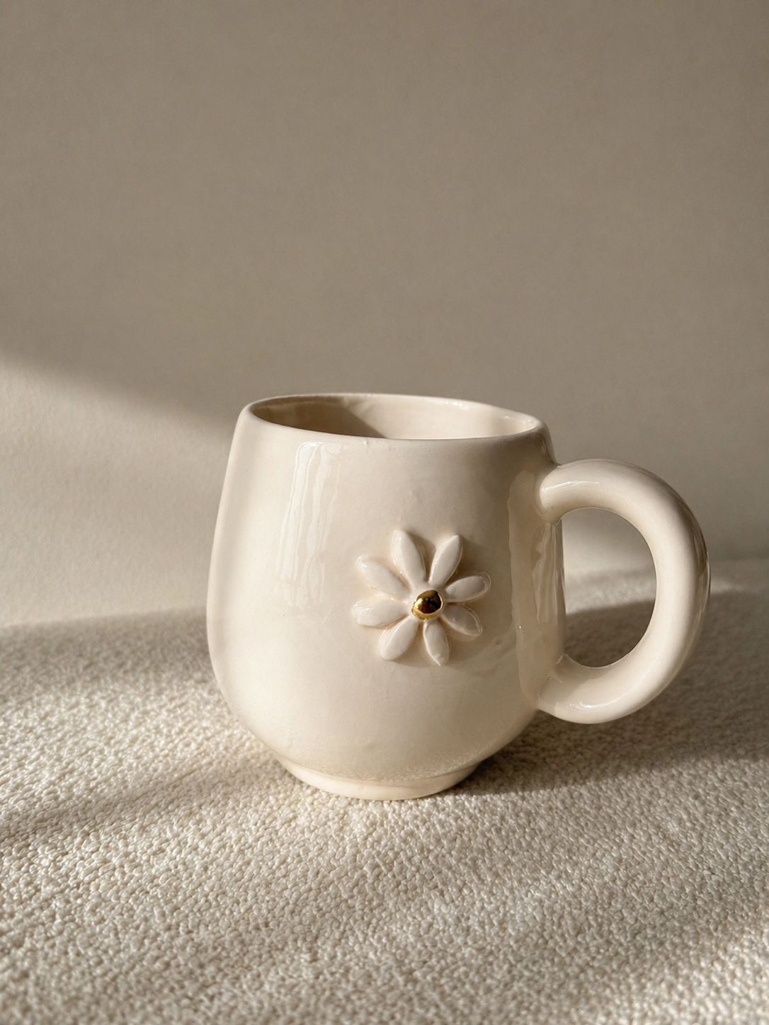 Taza de cerámica blanca con un detalle floral en el lateral, colocada sobre una superficie texturizada bajo una luz tenue.