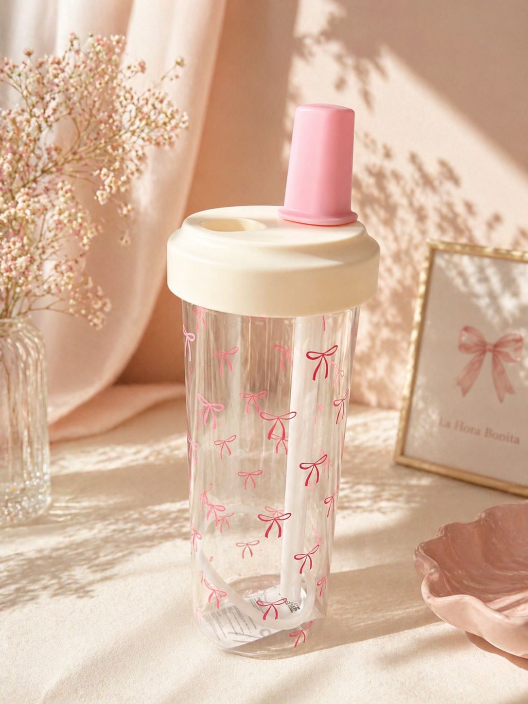 Botella transparente con tapón rosa y estampado de lazo sobre una mesa de tonos pastel suaves, iluminada por una cálida luz solar.