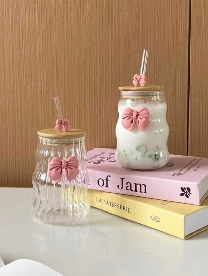 Dos velas decoradas en tarros de cristal con lazos rosas, apiladas sobre libros con un fondo de madera.